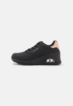 Sort Skechers sneakers med snørebånd, polstret sål, synligt luftkammer og beige accent på hælen.