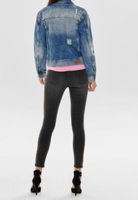 Ljusblå jeansjacka med slitna detaljer, kombinerad med en rosa topp och mörkgråa skinny jeans, kompletterad med svarta högklackade skor.