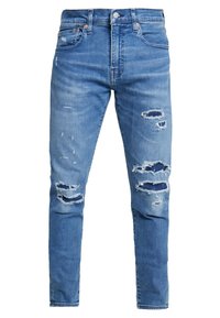 Blå denimjeans med slitna lappar och fransade kanter. Har en klassisk passform, fem fickor och metallfästen i midjan.