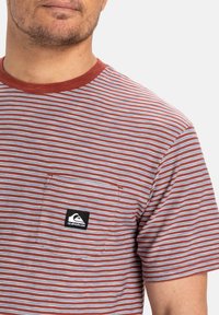 Gestreept t-shirt met een rode kraag, voorzien van dunne blauwe en witte horizontale strepen. Inclusief een linkse borstzak met een logo-patch.