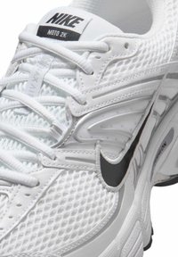 Bílé tenisky Nike mají síťovanou svrchní část, texturované detaily, výrazné černé logo Swoosh a polstrovaný límec pro podporu.