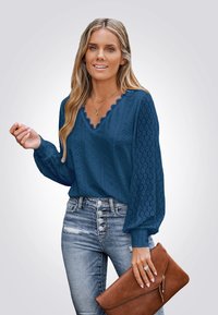 Marineblauwe blouse met een geschulpte V-hals en een getextureerd patroon, gecombineerd met hoogwaisted versleten denim en een bruine clutch.