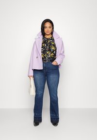 Casaco de lã lilás, blusa preta com padrão floral, jeans de ganga azul de cintura alta e flare, cinto preto e bolsa branca trançada. Texturas suaves, ajuste elegante.