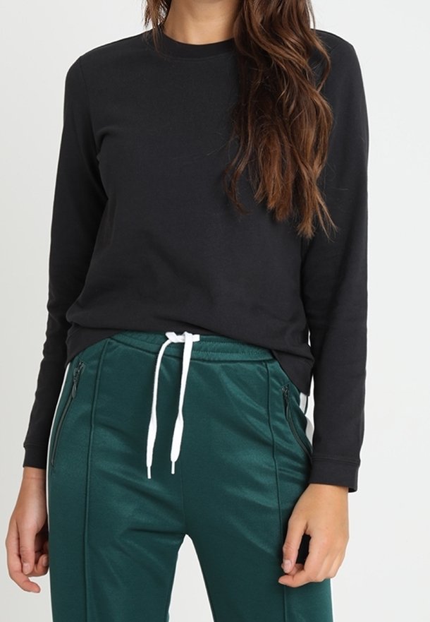 Maglietta nera a maniche lunghe abbinata a pantaloni verdi con vita elastica, caratterizzati da lacci bianchi e tasche laterali con zip.