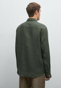 Green linen shirt with a collar, long sleeves, and buttoned cuffs. Smooth texture and straight hem, featured from the back view.