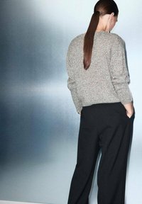 Suéter gris de punto con patrón texturizado, combinado con pantalones negros holgados. El modelo tiene el cabello largo recogido, contra un fondo claro.