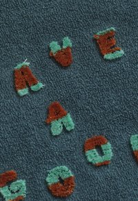 Textiel met getufte letters in oranje en groen die delen van "AVE," "AA," en "GO" spellen op een gestructureerde donkerblauwe stofachtergrond.