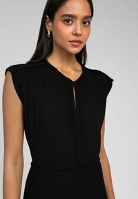 Robe noire avec une texture plissée, un col rond, des détails tressés et des manches courtes, avec une fermeture à boutons à l'avant.