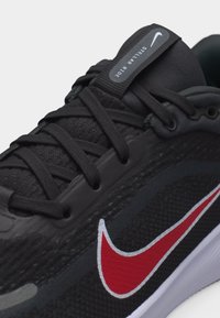 Κοντινό πλάνο μαύρου παπουτσιού τρεξίματος Nike με κόκκινο σήμα Swoosh, μαύρα κορδόνια και ετικέτα "Stellar Ride" στη γλώσσα, σε λευκό φόντο.