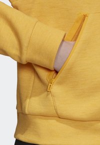 Žlutá mikina s texturovanou látkou, která má na boku kapsu na zip, žebrované manžety a přiléhavý střih.