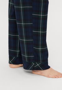 Laivastonsinisiä ruudullisia yöhaalareita, joissa on valkoisia ja vihreitä viivoja, pehmeä tekstuuri ja helman korostukset. Muotoilussa on avoin hihansuu alaosassa.