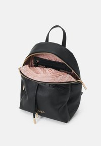 Zwarte leren rugzak met gouden rits geopend, onthullend een interieur van roze met een patroon en een zwarte ritsvak binnenin.