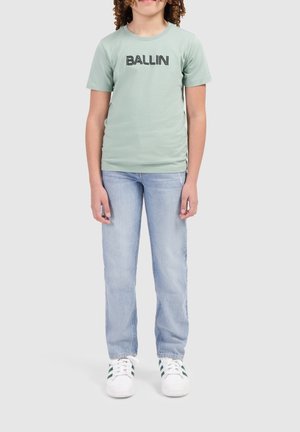 Lichtgroene katoenen t-shirt met "BALLIN" in vette zwarte letters gedrukt, gecombineerd met lichtblauwe spijkerbroek en witte sneakers met groene accenten.