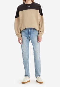 Beige och svart färgblockerad sweatshirt med rund halsringning, kombinerad med ljusblå jeans med slitna detaljer. Beiga sneakers.