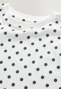 Valge kangas ühtlaselt paigutatud väikeste mustade täppidega ja ümar kaelus.