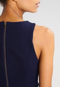 Marinblå ärmlös klänning med mjukt tyg och en synlig metalldragkedja bak, med en figurnära design och rena linjer.