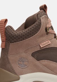 Scarpa alta in suede marrone e rete con suola in gomma, caratterizzata da accenti del logo e un'etichetta impermeabile. Include un colletto testurizzato e lacci.