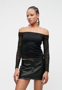 Top negru cu umeri la vedere, cu mâneci lungi din dantelă, corp neted și model floral. Asortat cu o fustă mini din piele neagră.