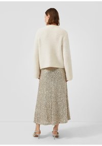 Cremefarbener, flauschiger, cropped Pullover kombiniert mit einem knielangen, schimmernden Rock aus goldenen Pailletten. Strappy beige High Heels runden das Outfit ab.