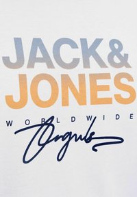 Valge puuvillane T-särk, millel on suur halli ja oranži gradueeritud "JACK & JONES" tekst, allpool on "WORLDWIDE" ja musta allkirja stiilis tekst.