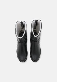Bottes en cuir noir avec doublure en fausse fourrure, fermeture éclair en haut, bout arrondi et texture lisse. Dotées d'un petit talon et d'une semelle robuste.