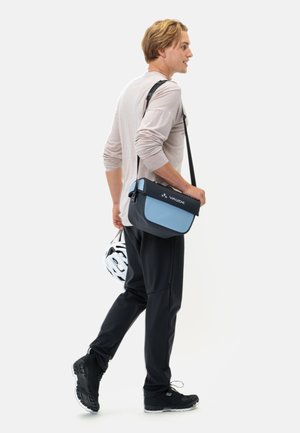 Borsa a tracolla blu e nera con chiusura a patta e logo, indossata a tracolla. La tracolla e l'esterno mostrano un design elegante e moderno.