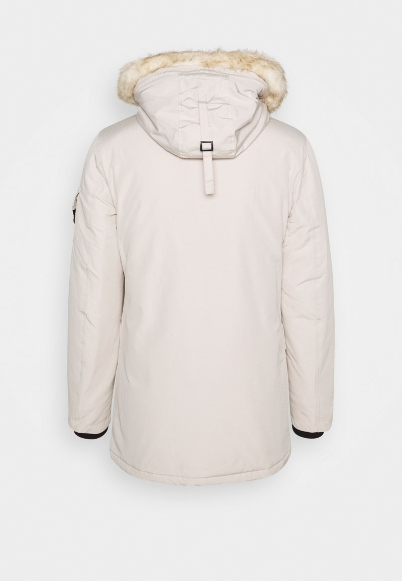 Parka crème avec une capuche en fourrure, présentant un design mi-long, des poches latérales et des poignets élastiques pour un ajustement confortable. Texture de tissu lisse.