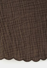 Tissu marron texturé avec un motif froissé et un bord festonné en bas sur fond blanc.