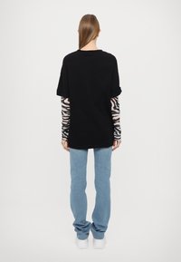 Svart oversized t-skjorte med korte oppbrettede ermer, lagdelt over lange gjennomsiktige ermer med zebramønster. Blå denimjeans og hvite sko.