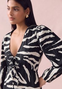 Black and white zebra-striped dress with a deep V-neck, tied waist, and puffed long sleeves, featuring a soft texture and flowing design.