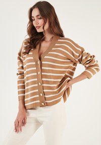 Cardigan rayat în nuanțe de bej și alb, cu decolteu în V adânc, croială oversized și nasturi aurii pe față. Material moale din tricot cu manșete ribelate.