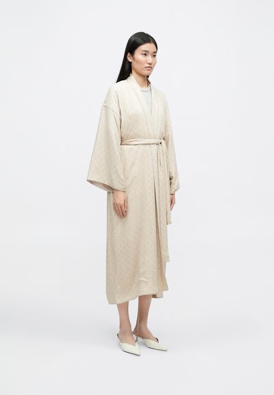 Μπεζ καμπούρα με σχέδιο και φαρδιές μανίκες, δεμένη στη μέση. Λείος υφασμάτινος χαρακτήρας, μήκους γόνατος με διακριτό σχέδιο ρόμβου και ζωνάκι.