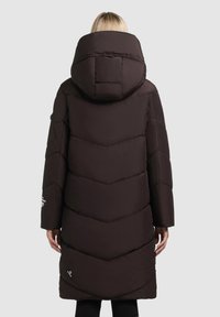 Garšs, tumši brūns pūkains mētelis ar lielu kapuci, vertikāliem chevron šuvēm un sānu kabatām. Siluets ir brīvs un izolēts.