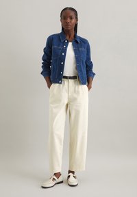 Blauwe denimjack met twee borstzakken, witte t-shirt, crèmekleurige wijde broek en witte schoenen met gespsluiting. Minimalistische stijl.