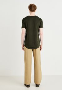 Tricou scurt de culoare verde închis, cu un croi lejer, guler rotund, asociat cu pantaloni largi de culoare bej deschis și cizme negre. Design simplu.