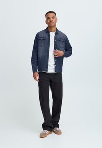 Donkerdenim overhemd met knoopsluiting aan de voorkant, twee borstzakken en lange mouwen. Gepaarde met zwarte broek en grijze sneakers met witte strepen.
