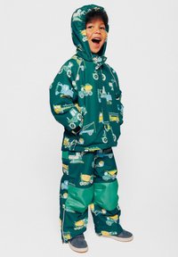 Giacca e pantaloni impermeabili verdi con motivo a veicoli da costruzione gialli e blu. Include un cappuccio e zip all'orlo dei pantaloni.