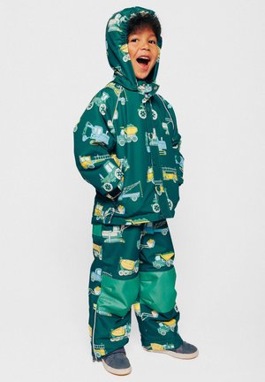 Giacca e pantaloni impermeabili verdi con motivo a veicoli da costruzione gialli e blu. Include un cappuccio e zip all'orlo dei pantaloni.