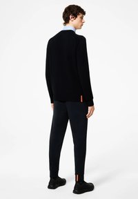 Marine gebreide trui met geribbelde manchetten en zoom, gecombineerd met marine tapered broek met een oranje accent bij de enkel. Zwarte sportieve schoenen.