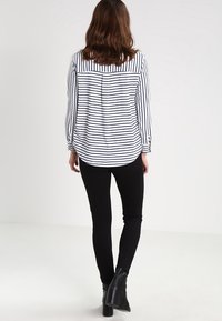 Pruhovaný černo-bílý dlouhý rukáv blůza s kulatým výstřihem, detailem sklady na zádech a černými přiléhavými kalhotami, doplněná kotníkovými botami.
