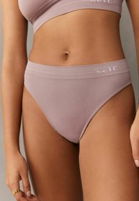 Ljus mauve bikini med bred midjeband, sömlös design och subtil logotyp på framsidan. Slät textur och åtsittande form.