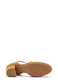 Scarpa in suede marrone con tacco a blocco, caratterizzata da una punta rotonda e una cinghia alla caviglia. La suola è texturizzata per garantire aderenza.