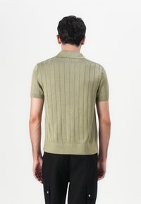 Kortärmad polo i ljusgrön ribbad trikå med krage, med strukturerade vertikala ränder och en figurnära siluett.