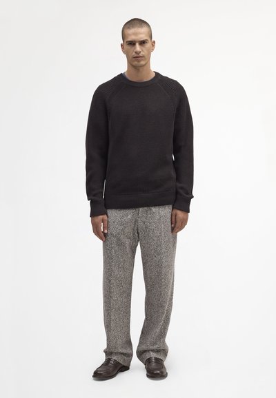 Donkere gebreide trui met geribbelde manchetten, gecombineerd met lichtgrijze gestructureerde broek en bruine schoenen. Eenvoudig ontwerp, neutrale kleuren.