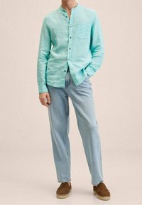 Licht turquoise linnen overhemd met een knoopsluiting aan de voorkant en een borstzak, gecombineerd met lichtblauwe jeans en bruine espadrilles.