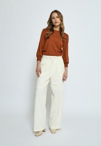 Pull en maille marron avec des manches bouffantes, associé à un pantalon large taille haute blanc et des mules à talons beiges. Design simple, textures lisses.