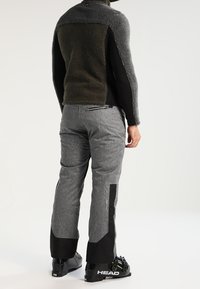 Tenue masculine avec une veste en polaire grise dotée d'un panneau inférieur noir et d'un pantalon gris texturé. Des bottes de ski noires complètent le look.