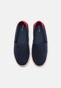 Navy canvas slip-on kengät, joissa on punaiset yksityiskohdat, juuttireunus ja teksturoitu pinta. Varustettu joustavilla sivupaneeleilla helppoa pukeutumista varten.