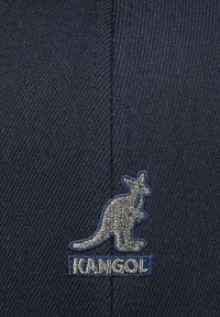 Cappello blu navy realizzato in tessuto texture, con un logo di un canguro argentato e il testo "KANGOL" sottostante. Forma classica con dettagli di cucitura visibili.