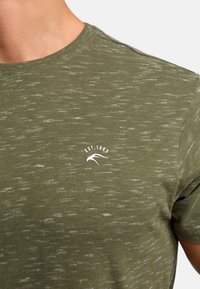 Oliwkowa koszulka z teksturowanym wykończeniem, z białym logo "EST. 1993" na piersi. Klasyczny krój z okrągłym dekoltem.